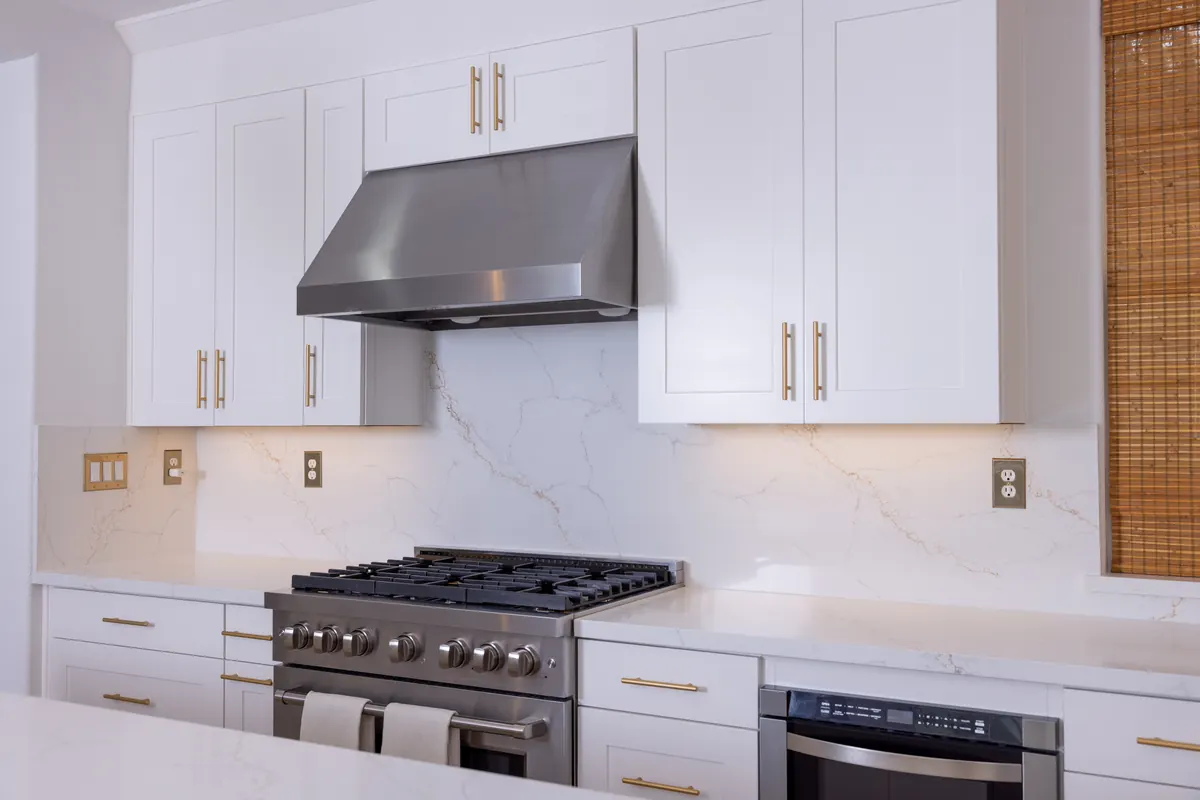 White shaker cabinets with brass pulls and quartz backsplash