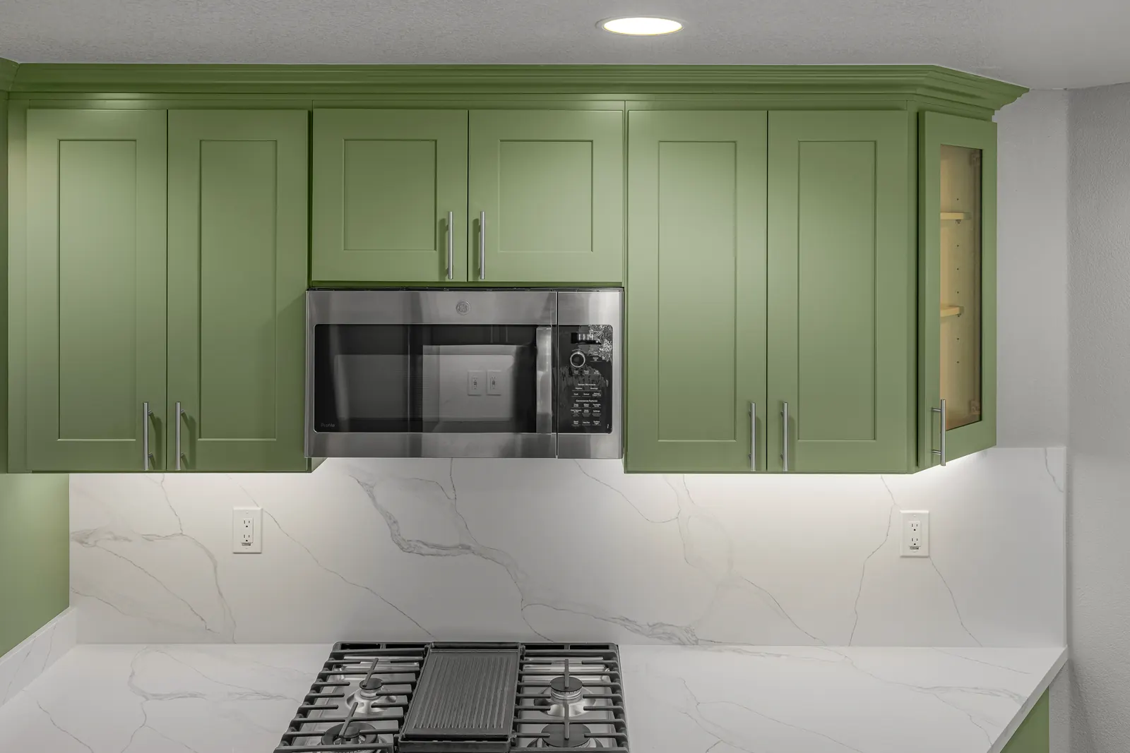 Green upper cabinets with stainless microwave and quartz backsplash